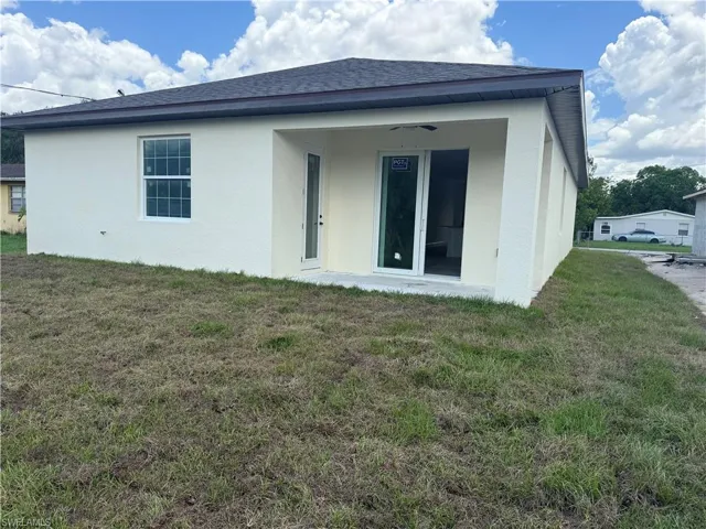 Rear view of house with stucco siding, a lawn, and a shingled roof