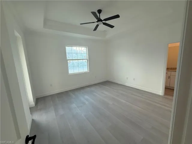 Unfurnished room featuring a raised ceiling, wood finished floors, crown molding, and ceiling fan