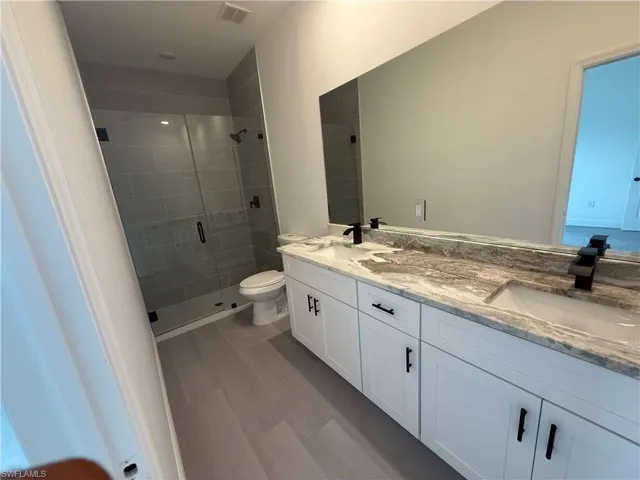 Bathroom featuring a stall shower, double vanity, and wood finished floors