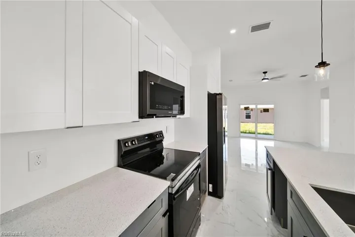 Kitchen featuring black appliances, light marble finish flooring, decorative light fixtures, light stone counters, and open floor plan