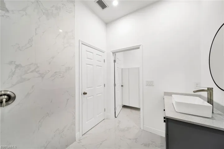 Full bathroom with double vanity, light marble finish flooring, and recessed lighting