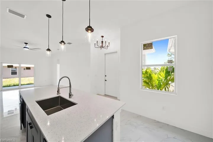 Kitchen with light marble finish flooring, pendant lighting, light stone counters, a kitchen island with sink, and a chandelier