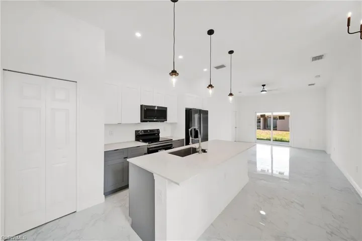 Kitchen with white cabinets, pendant lighting, black appliances, a center island with sink, and recessed lighting