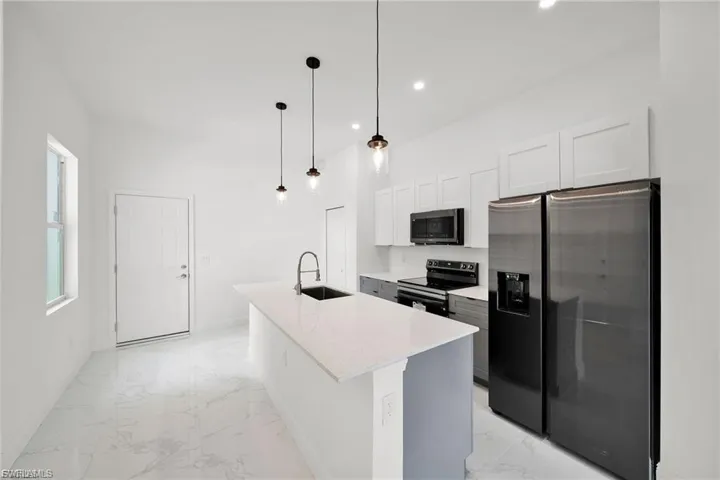 Kitchen with appliances with stainless steel finishes, white cabinetry, light marble finish flooring, a center island with sink, and recessed lighting