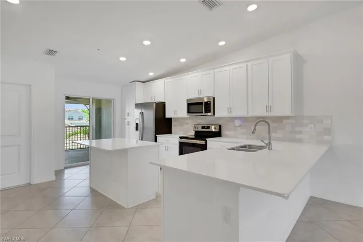 Kitchen with stainless steel appliances, island, tiled backsplash, quartz countertops