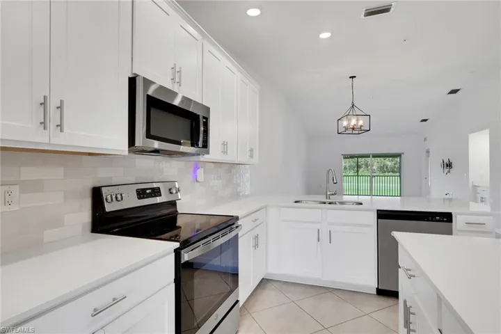 Kitchen with stainless steel appliances, tiled backsplash, quartz countertops