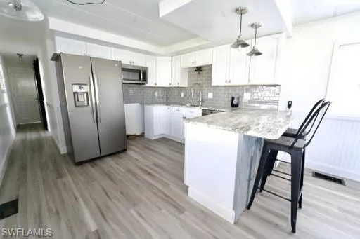 Contemporary kitchen featuring white cabinetry, a light gray tile backsplash, stainless steel appliances, a breakfast bar with stone-finish countertop, and wood-finish flooring