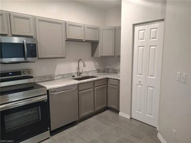 Kitchen with gray cabinetry, stainless steel appliances, and light stone counters