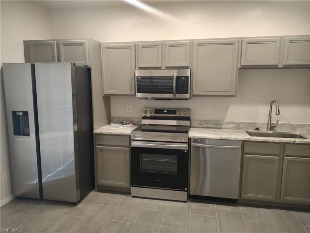 Kitchen featuring gray cabinetry, stainless steel appliances, and light stone countertops