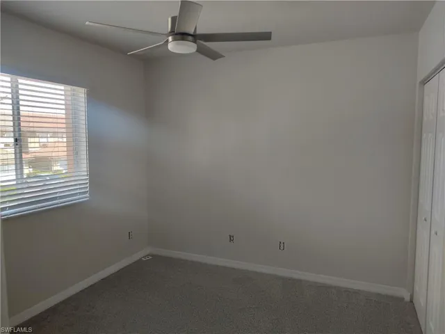 Spare room featuring a ceiling fan and dark colored carpet
