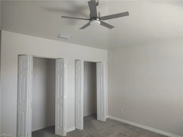 Unfurnished bedroom featuring dark carpet, multiple closets, and a ceiling fan