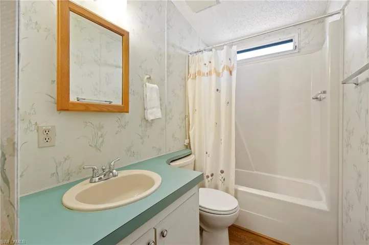 Full bath with vanity, toilet, a textured ceiling, shower / bath combo with shower curtain, and wallpapered walls