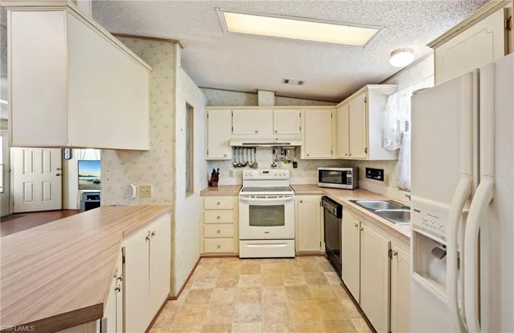 Kitchen with lofted ceiling, white appliances, wallpapered walls, light countertops, and a textured ceiling