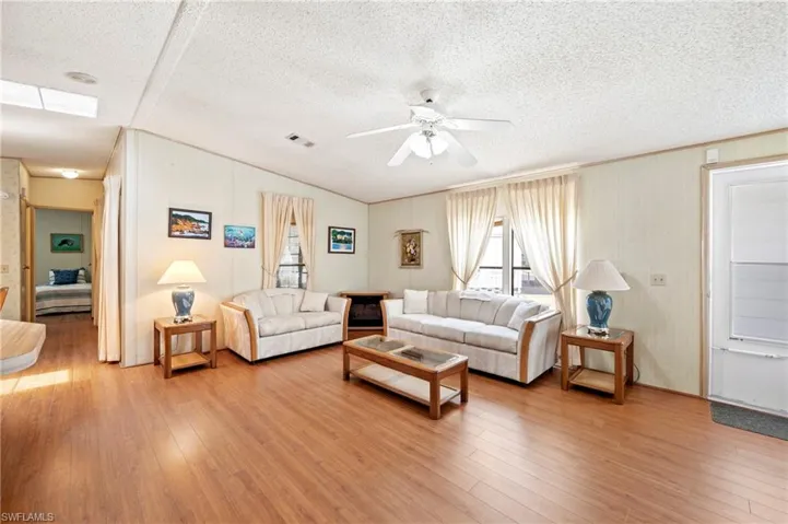 Living room with ceiling fan, a textured ceiling, wood finished floors, lofted ceiling, and visible vents