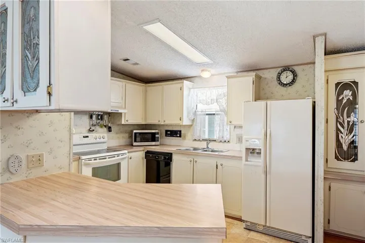 Kitchen featuring a sink, wallpapered walls, white appliances, and visible vents