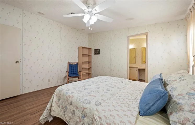 Bedroom with a ceiling fan, a textured ceiling, wood finished floors, wallpapered walls, and ensuite bath