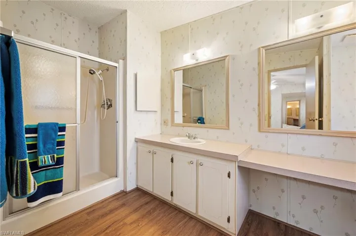 Full bath featuring a textured ceiling, a stall shower, wood finished floors, vanity, and wallpapered walls