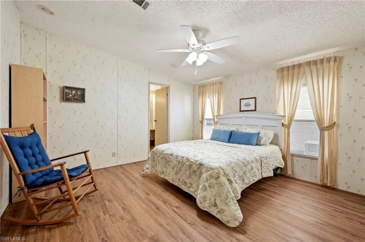 Bedroom with light wood-style floors, a textured ceiling, visible vents, and wallpapered walls