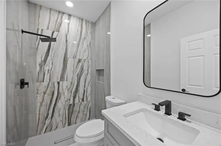 Bathroom featuring toilet, a marble finish shower, and vanity