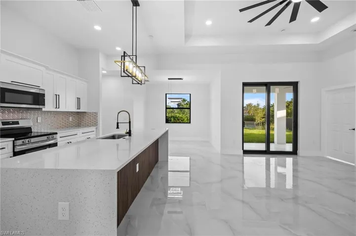 Kitchen featuring stainless steel appliances, a sink, tasteful backsplash, white cabinetry, and light marble finish floors