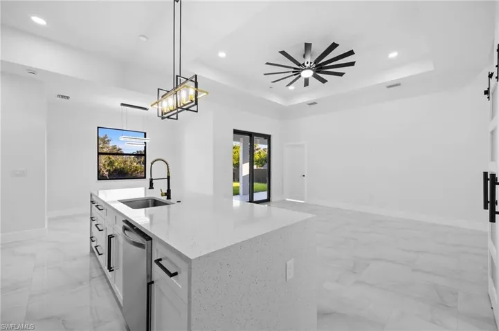Kitchen featuring a sink, stainless steel dishwasher, light marble finish floors, recessed lighting, and a kitchen island with sink