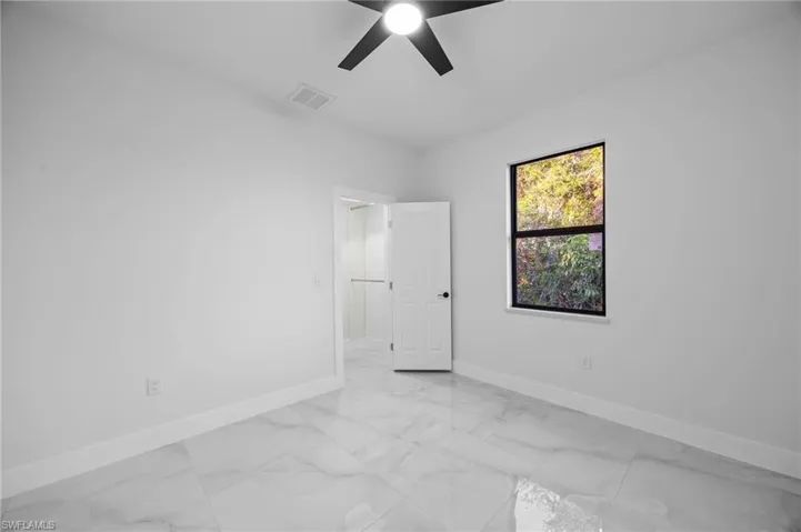 Empty room with baseboards, light marble finish floors, and a ceiling fan