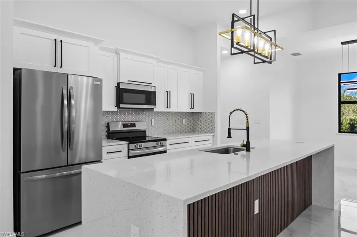 Kitchen featuring stainless steel appliances, a sink, white cabinets, backsplash, and a center island with sink