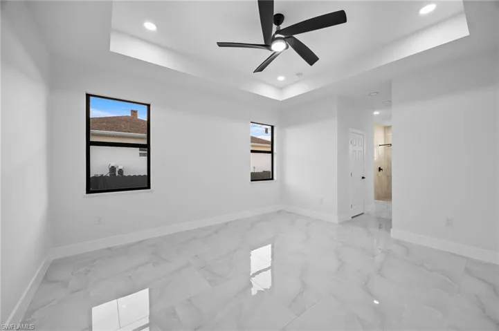 Unfurnished room featuring recessed lighting, a raised ceiling, healthy amount of natural light, light marble finish floors, and baseboards