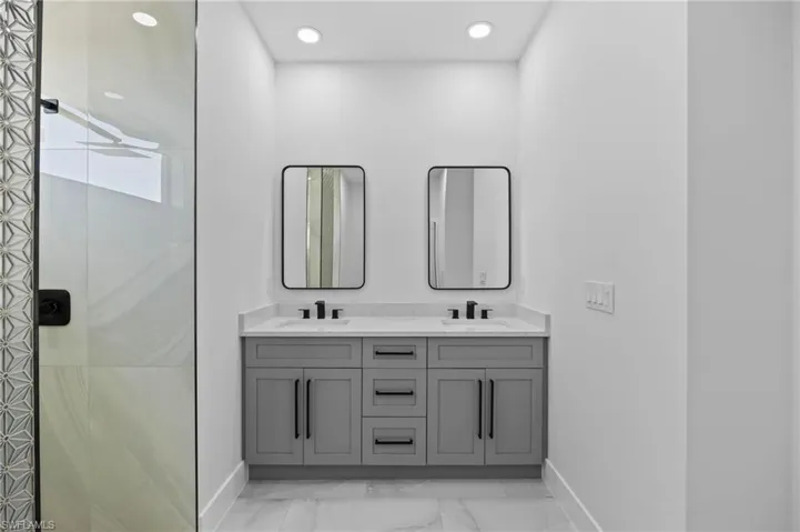 Bathroom with baseboards, marble look tile flooring, double vanity, a shower, and recessed lighting