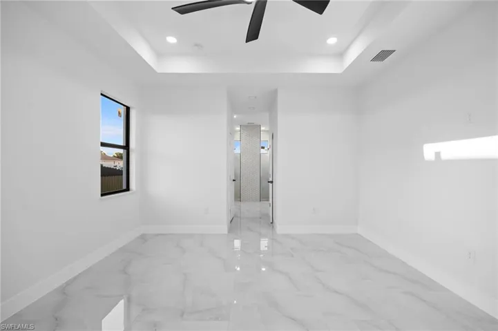 Unfurnished room featuring a tray ceiling, baseboards, ceiling fan, marble look tiles, and recessed lighting