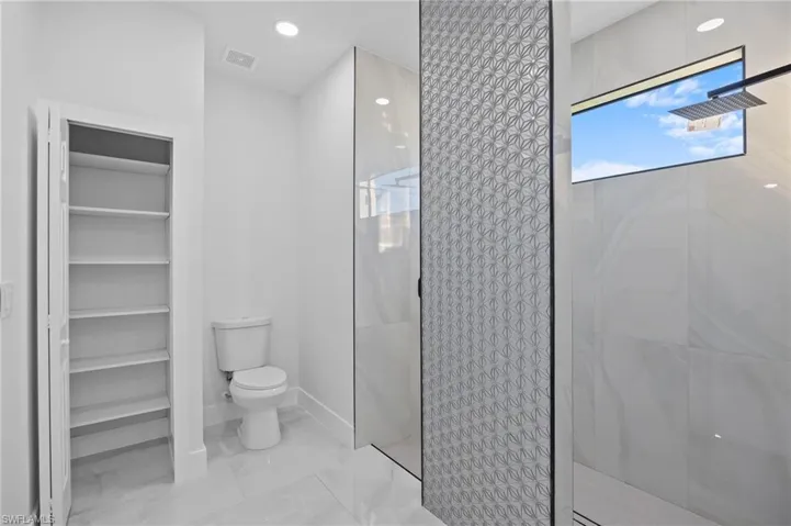 Bathroom featuring walk in shower, toilet, and marble look tiles