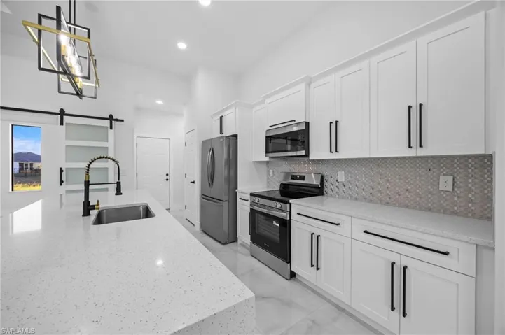 Kitchen with appliances with stainless steel finishes, a sink, backsplash, white cabinetry, and pendant lighting