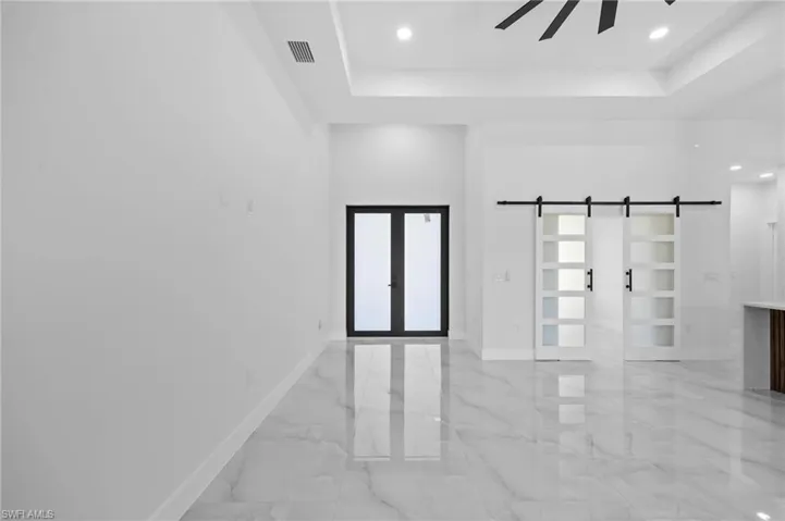 Empty room with french doors, a barn door, a raised ceiling, light marble finish floors, and baseboards