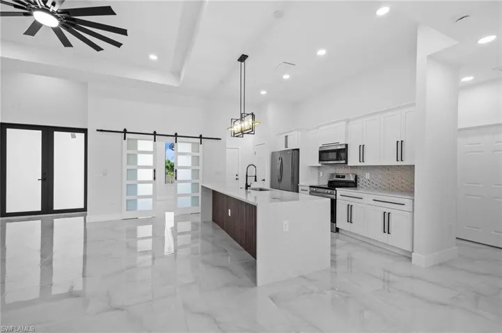 Kitchen featuring appliances with stainless steel finishes, a sink, light marble finish flooring, a high ceiling, and white cabinets