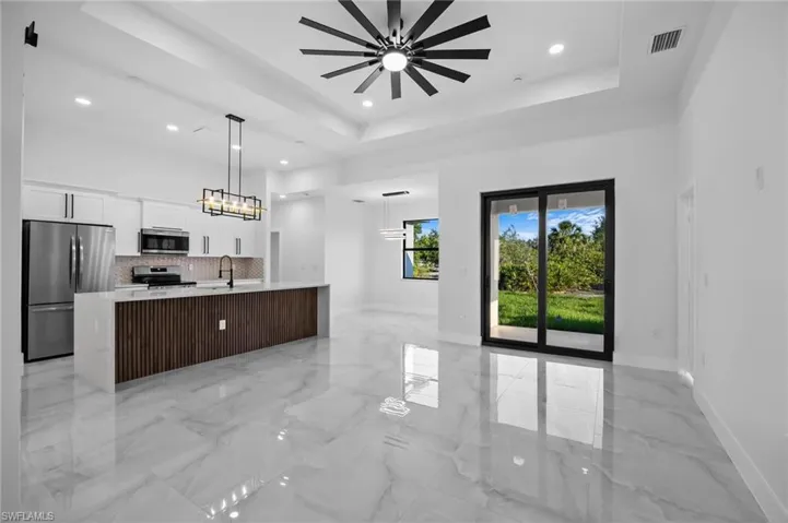 Kitchen with stainless steel appliances, a sink, a raised ceiling, white cabinetry, and a large island