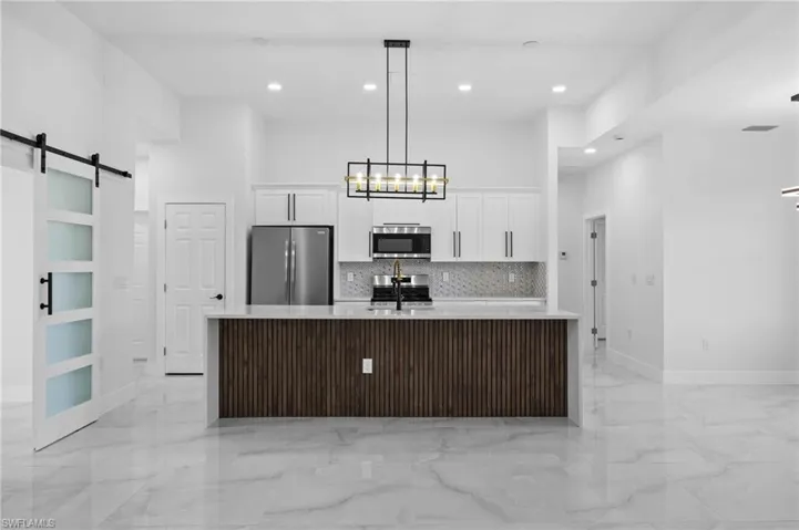 Kitchen featuring stainless steel appliances, light marble finish flooring, a barn door, white cabinetry, and a towering ceiling