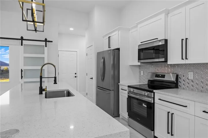 Kitchen with appliances with stainless steel finishes, a sink, white cabinetry, light stone counters, and recessed lighting