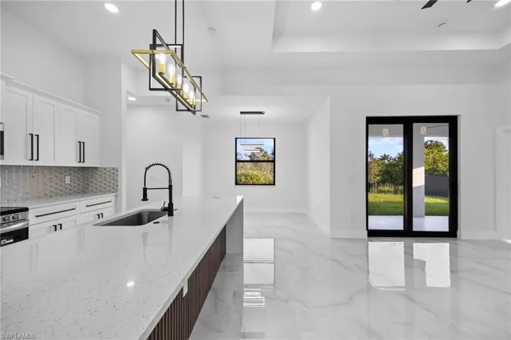 Kitchen with a sink, recessed lighting, light marble finish floors, backsplash, and white cabinets