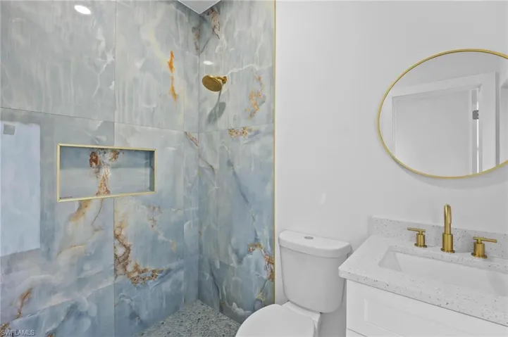 Full bath featuring a marble finish shower, vanity, and toilet