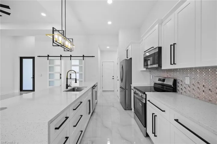Kitchen featuring appliances with stainless steel finishes, a sink, a barn door, a spacious island, and white cabinetry