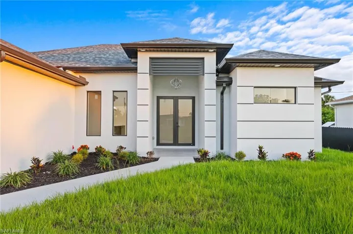 Doorway to property featuring stucco siding, roof with shingles, and a yard