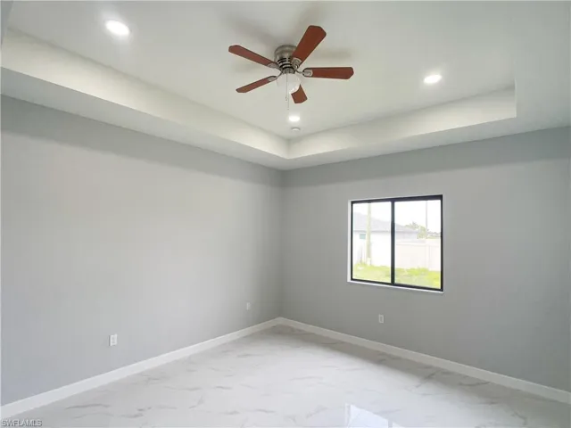 Unfurnished room featuring baseboards, recessed lighting, a ceiling fan, a tray ceiling, and marble finish floor