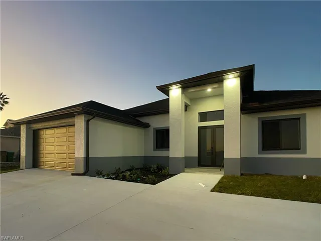 View of front of property featuring a garage, driveway, stucco siding, and french doors