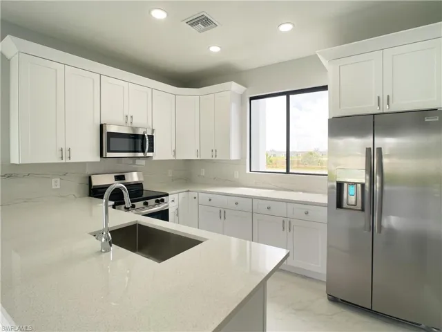 Kitchen with visible vents, a sink, appliances with stainless steel finishes, light stone countertops, and marble finish floor