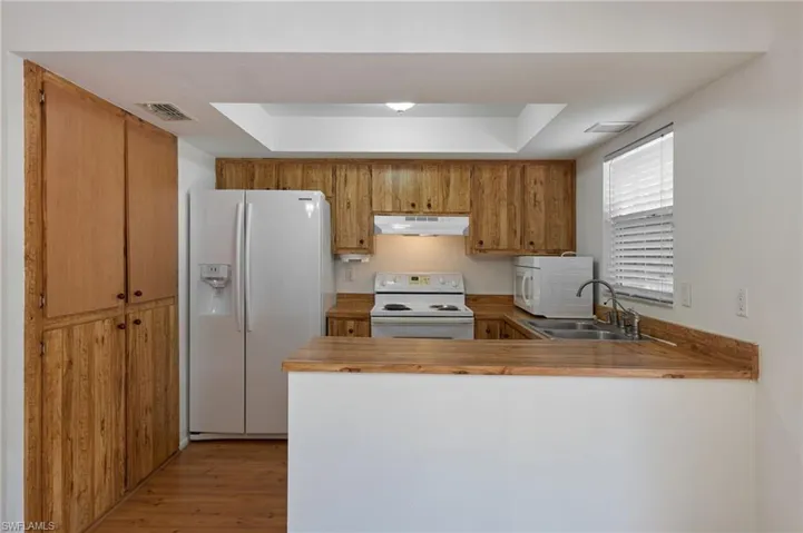 Kitchen with light hardwood / wood-style floors, sink, a raised ceiling, and white appliances
