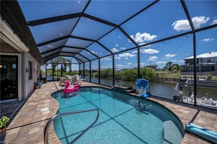 Heated saltwater pool featuring a waterfall, an extended patio, a water view, and screened in cage for comfort