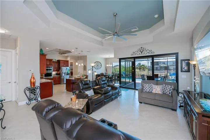 Living area featuring ceiling fan, a tray ceiling, plenty of natural light, and light tile patterned flooring