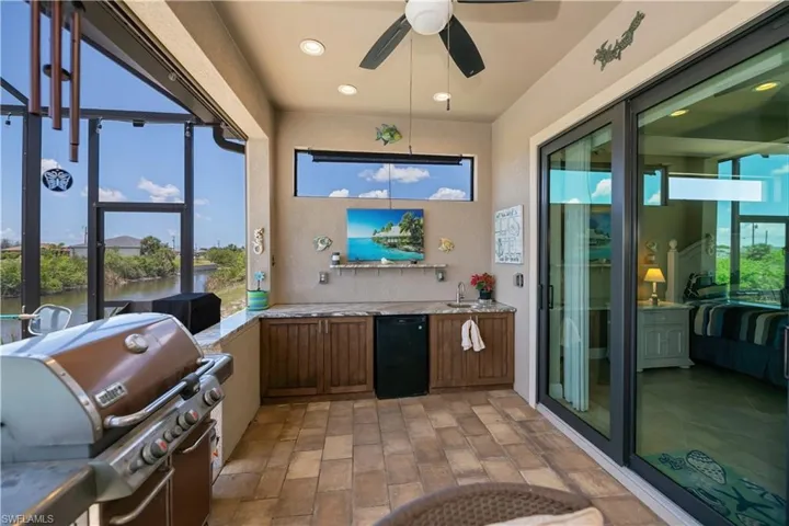 Patio with grilling area, a sink, outdoor fridge, a ceiling fan, and a water view