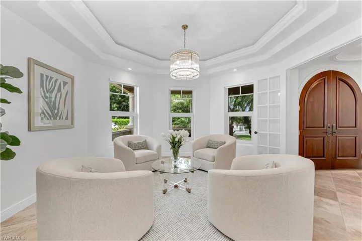 Living room featuring a tray ceiling, crown molding, an inviting chandelier, and baseboards