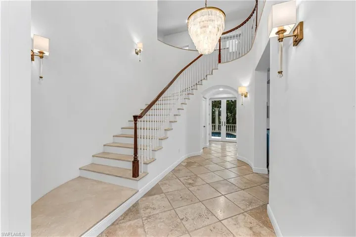 Foyer entrance featuring baseboards, arched walkways, a notable chandelier, stairway, and a towering ceiling